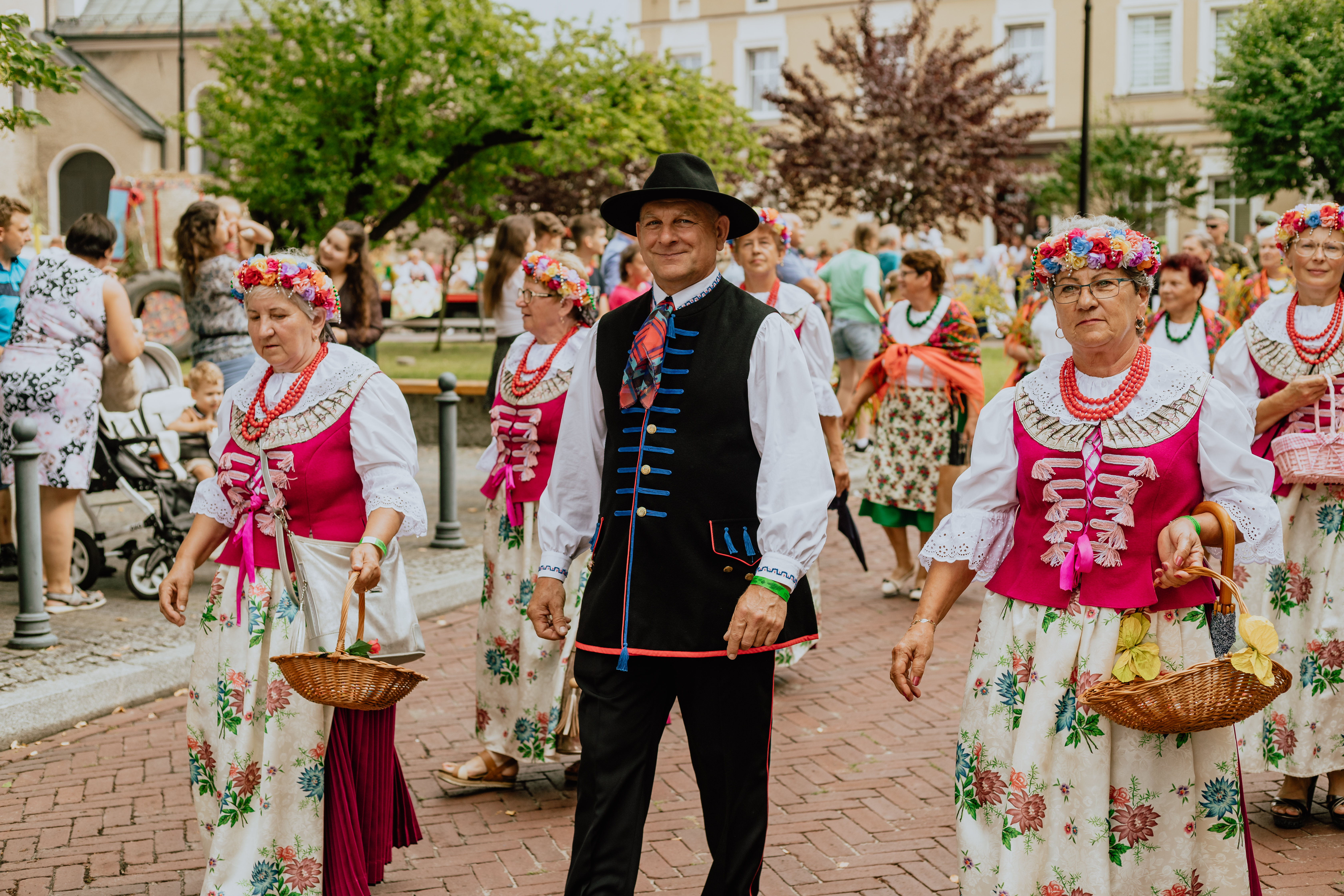 panie i pan w regionalnych strojach idą ulicą podczas dożynkowego korowodu